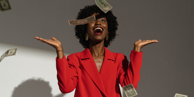 Happy woman in a red suit looking at cash money falling from the sky