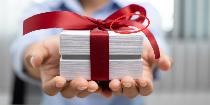 Close-up shot of a person handing you a gift box tied with red ribbon