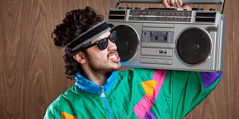 Young man with mullet and neon track suit holding a boom box on his shoulder