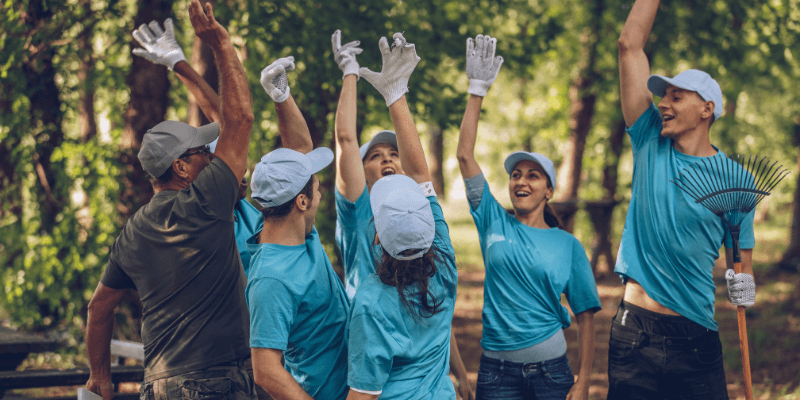 Six people raising their arms in the air while cheering in the forest while volunteering.